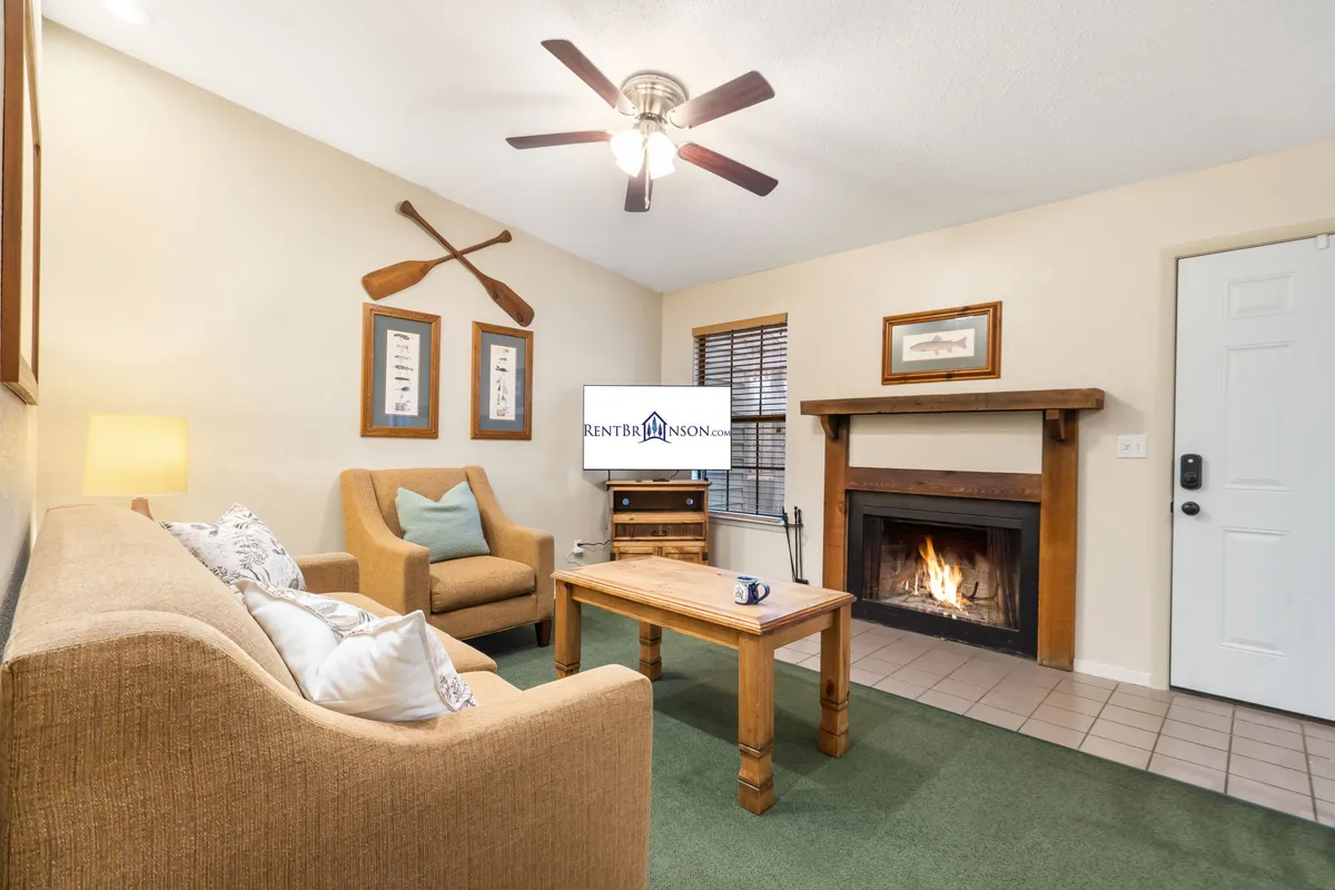 The image showcases a cozy living room with a glowing fireplace, a plush sofa, a coffee table perfect for games or snacks, a TV for entertainment, and stylish decorative oars on the wall, all set in a warm, inviting atmosphere.