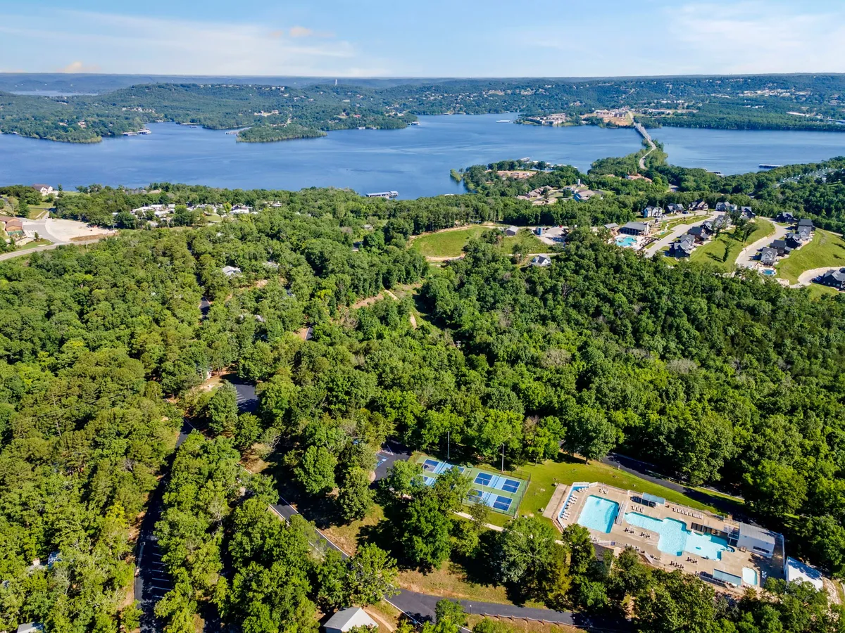 A sweeping view of the expansive lake is paired with the swimming pool area and tennis courts, set against lush greenery. The image suggests the diversity of recreational amenities available, from lake outings to resort activities.
