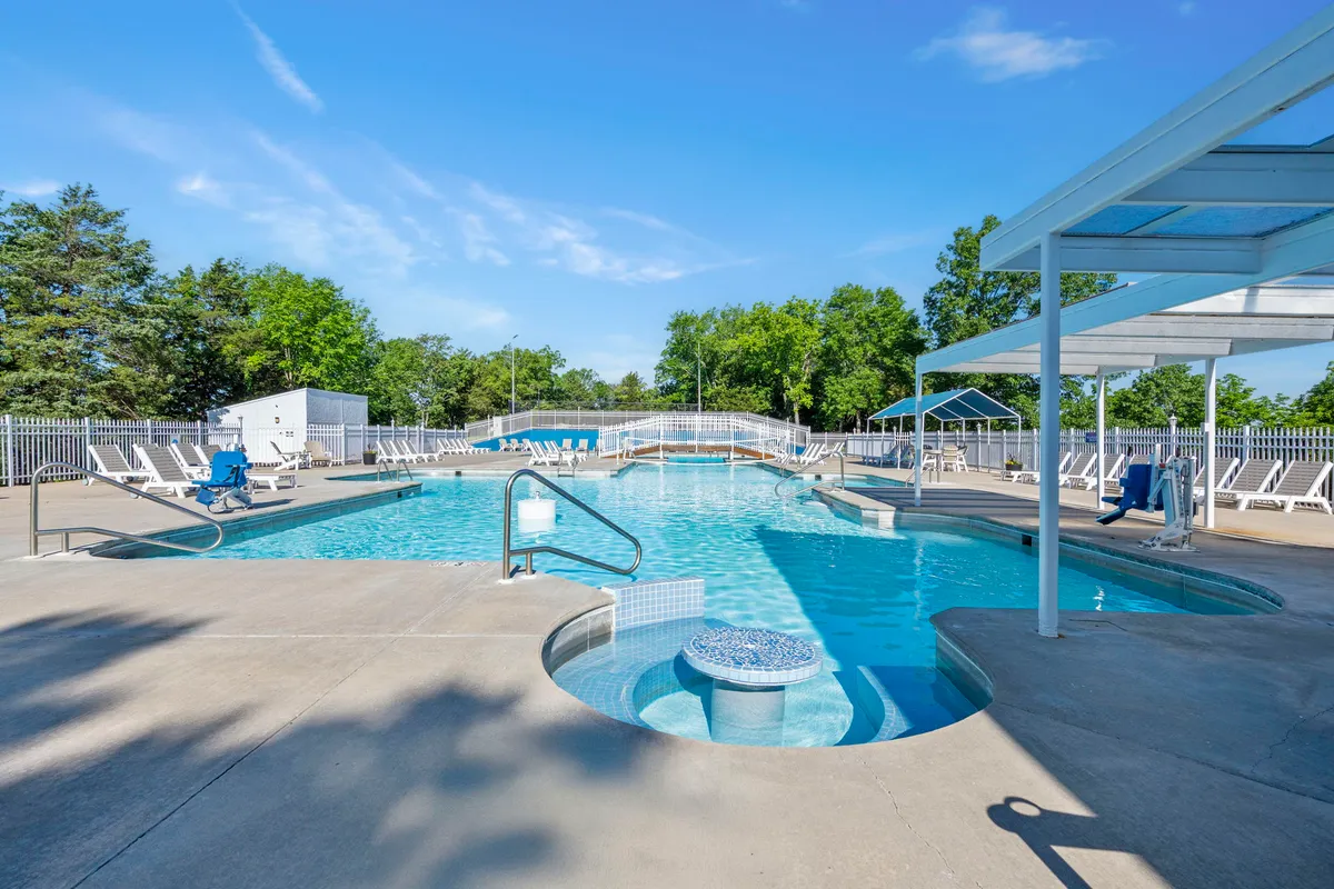A sparkling outdoor swimming pool bordered by lounge chairs and lush greenery. The area is lively and inviting, ideal for families to relax, swim, or enjoy a cheerful afternoon together. Hints of sunset lighting add a warm, fun-filled atmosphere to the space.