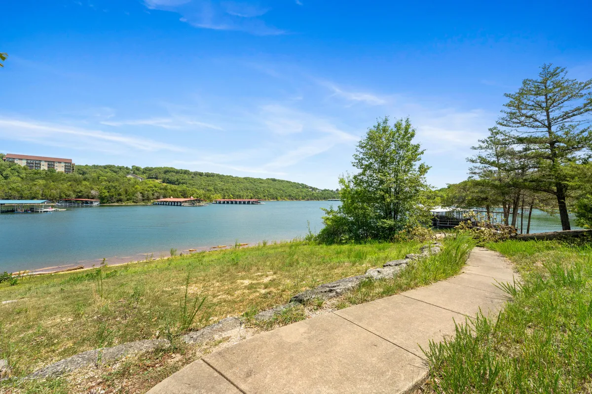 This exterior image features a peaceful lakeside scene with a winding pathway bordered by greenery, leading toward the water and with buildings visible in the background. The setting conveys a sense of tranquility and provides an inviting glimpse of the natural areas surrounding the retreat.