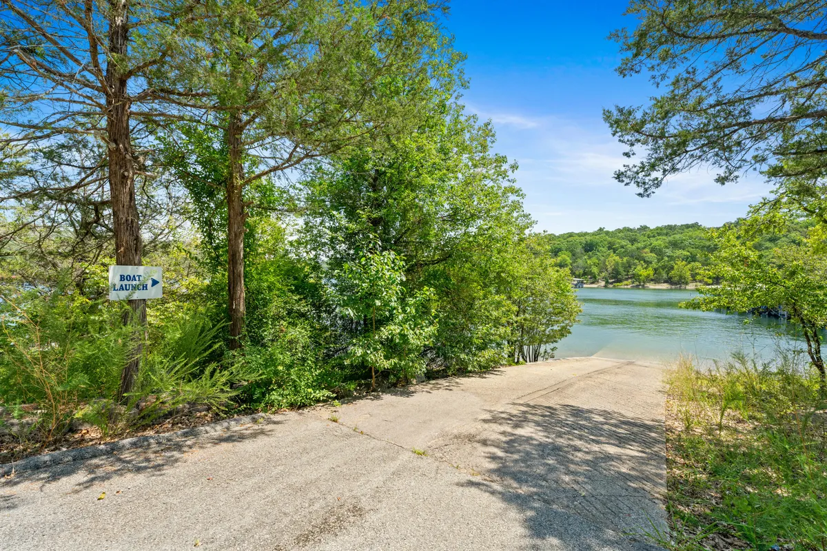 This exterior shot focuses on the boat launch area next to the waterfront, framed by lush greenery and calm water. A boat launch sign is clearly visible, and the natural setting is peaceful yet ready for adventure, perfect for starting a day on the water or returning after sunset.