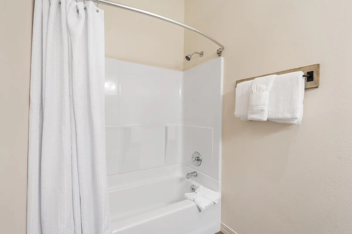 A pristine ensuite bathroom with a bathtub, shower curtain, and crisp towels neatly arranged. The space is bright and serene, ideal for relaxing after an active day.