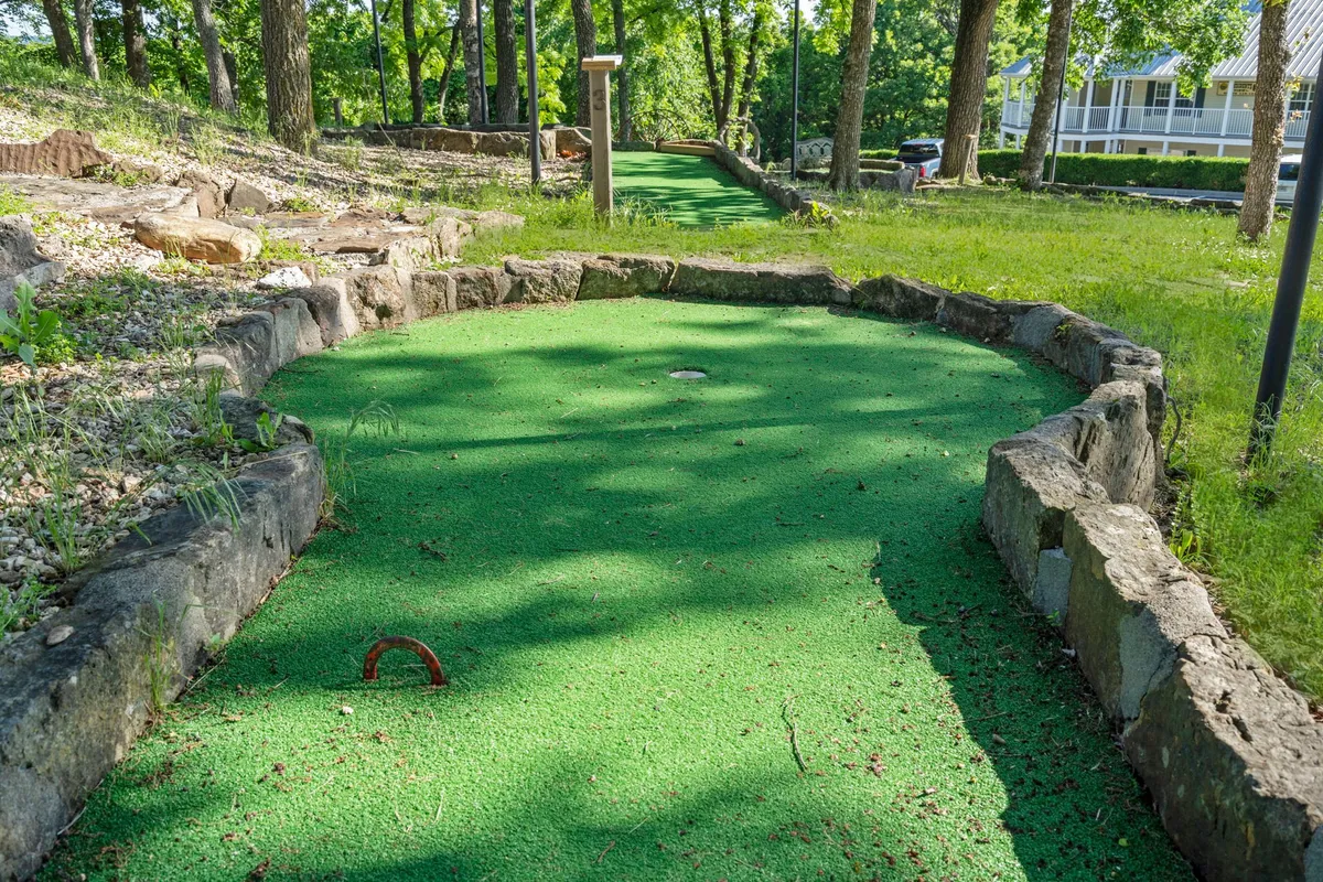 A cheerful mini-golf course winds through surrounding trees with stone borders, inviting families and friends to playful outdoor competition and relaxation.