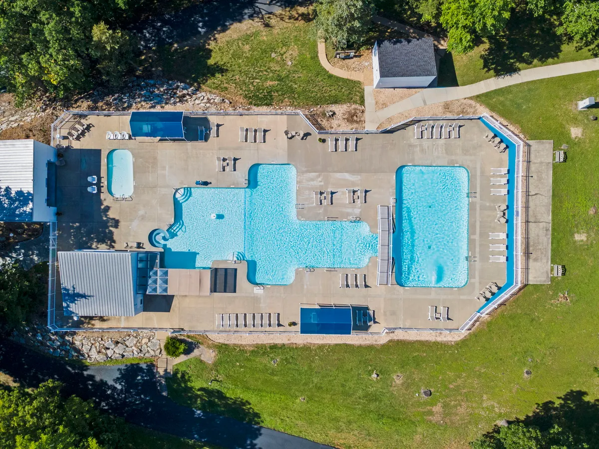 A vibrant pool area surrounded by lounge chairs, greenery, and a cabana, where guests can be seen swimming, sunbathing, and socializing. The atmosphere is relaxed and cheerful, ideal for family gatherings and cooling off on warm days.