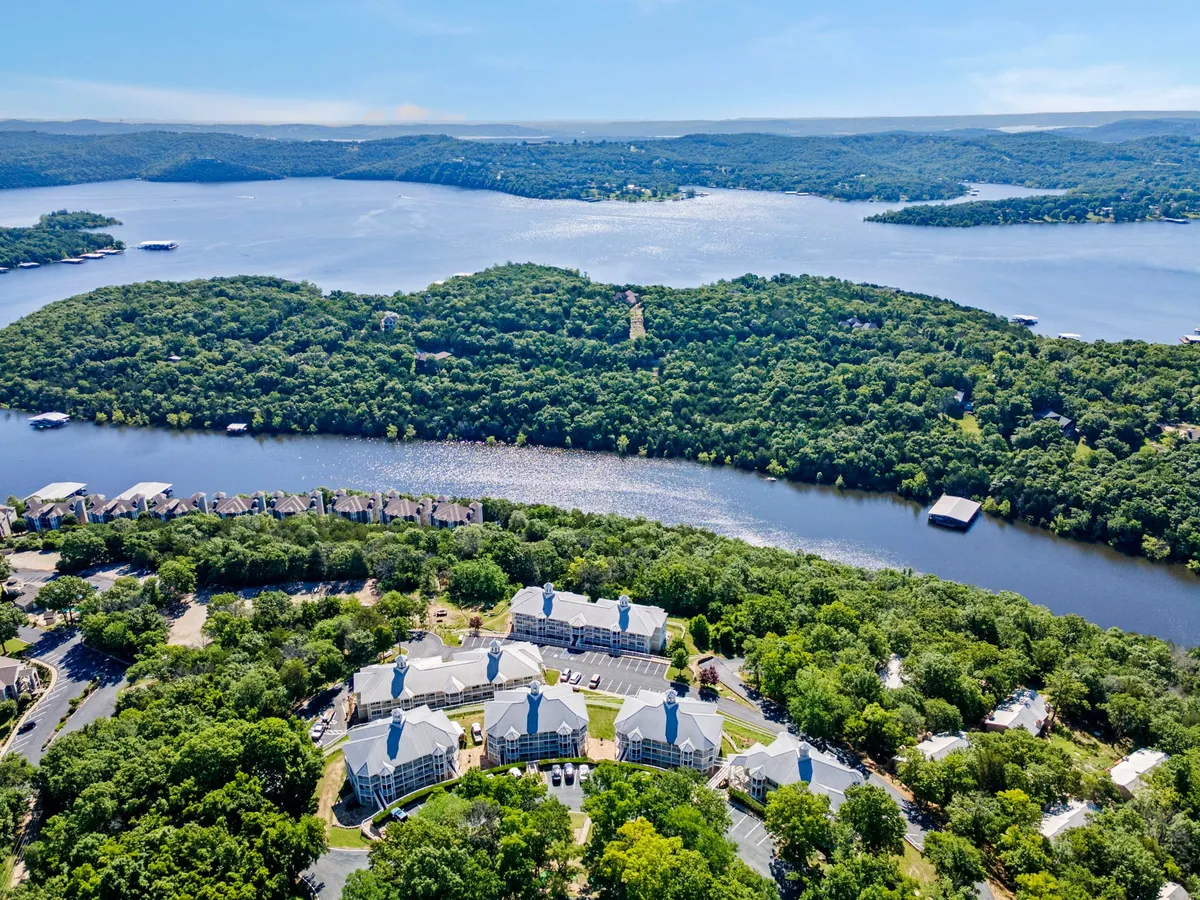 A panoramic view of Table Rock Lake surrounded by lush greenery and islands, with a visible cluster of resort buildings in the distance. The tranquil water is perfect for boating, fishing, or kayaking adventures, and the expansive sky hints at beautiful sunset vistas.