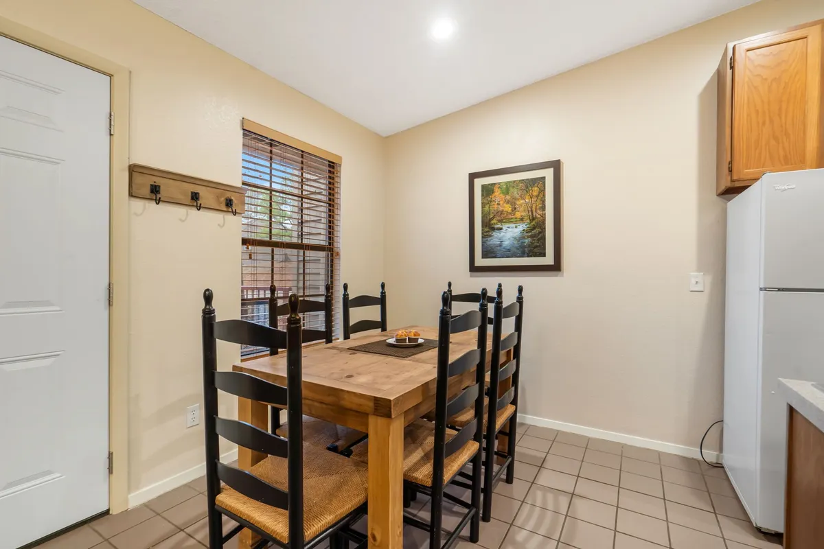 A classic dining area featuring a wooden dining table and chairs, wall art, and a glimpse of kitchen appliances, all bathed in warm, natural light. The scene exudes a sense of togetherness and everyday comfort.