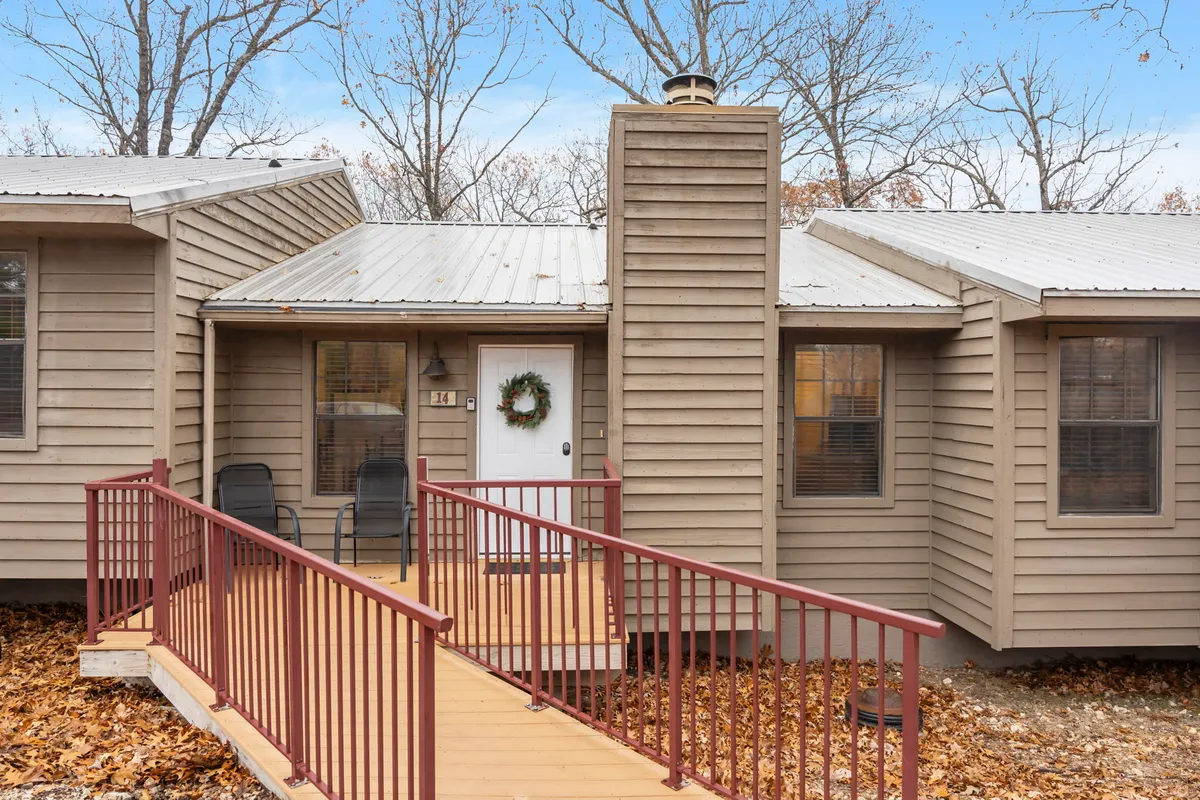 A welcoming exterior shot of the retreat’s entrance, featuring a front door adorned with a wreath, a distinctive red railing, and cozy porch seating. The scene is inviting, suggesting a comfortable and homey environment.