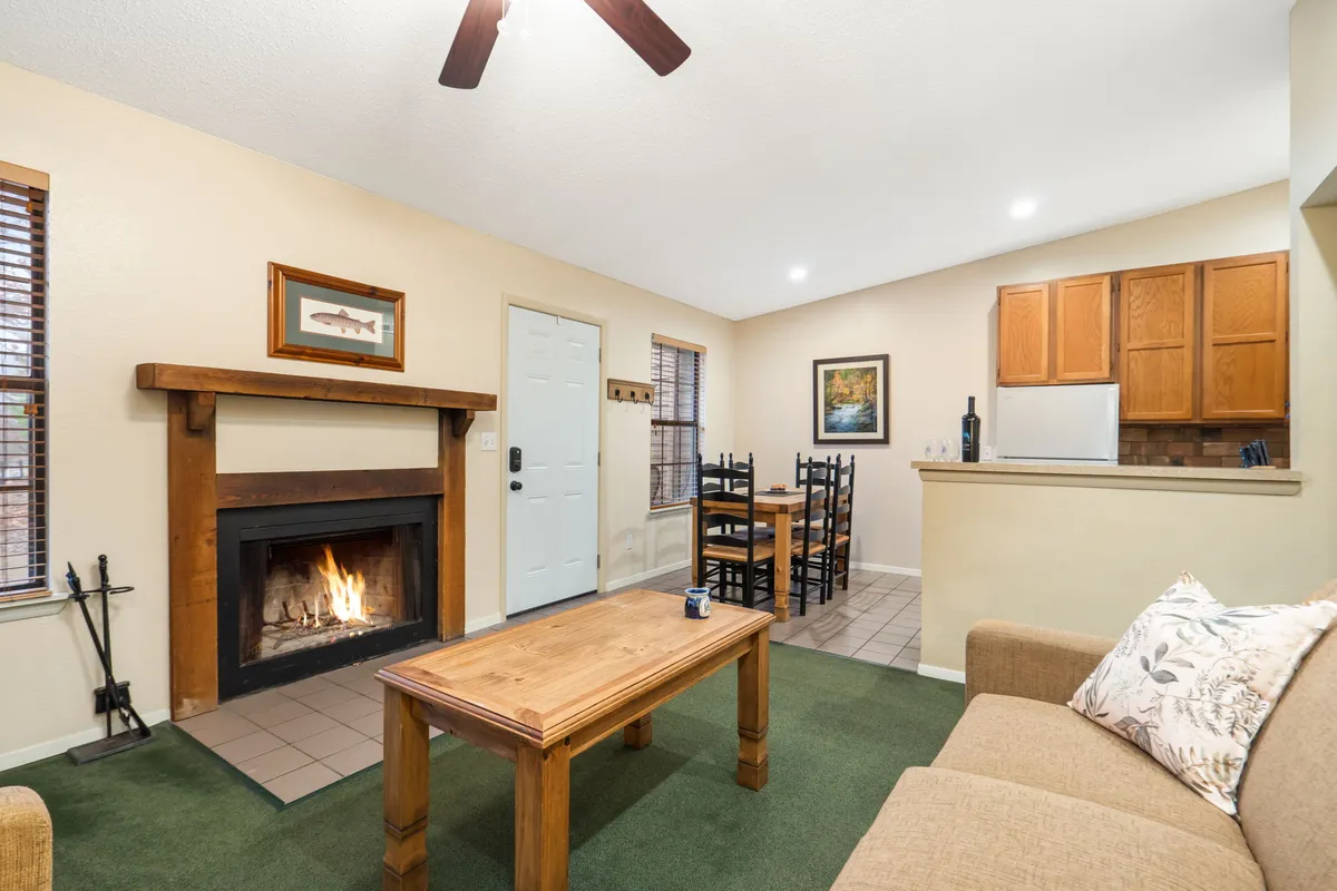 A welcoming open-plan living and dining space featuring a plush sofa, cozy fireplace, classic dining table, and artwork on the wall. Large windows let in abundant natural light, enhancing the warm ambiance.