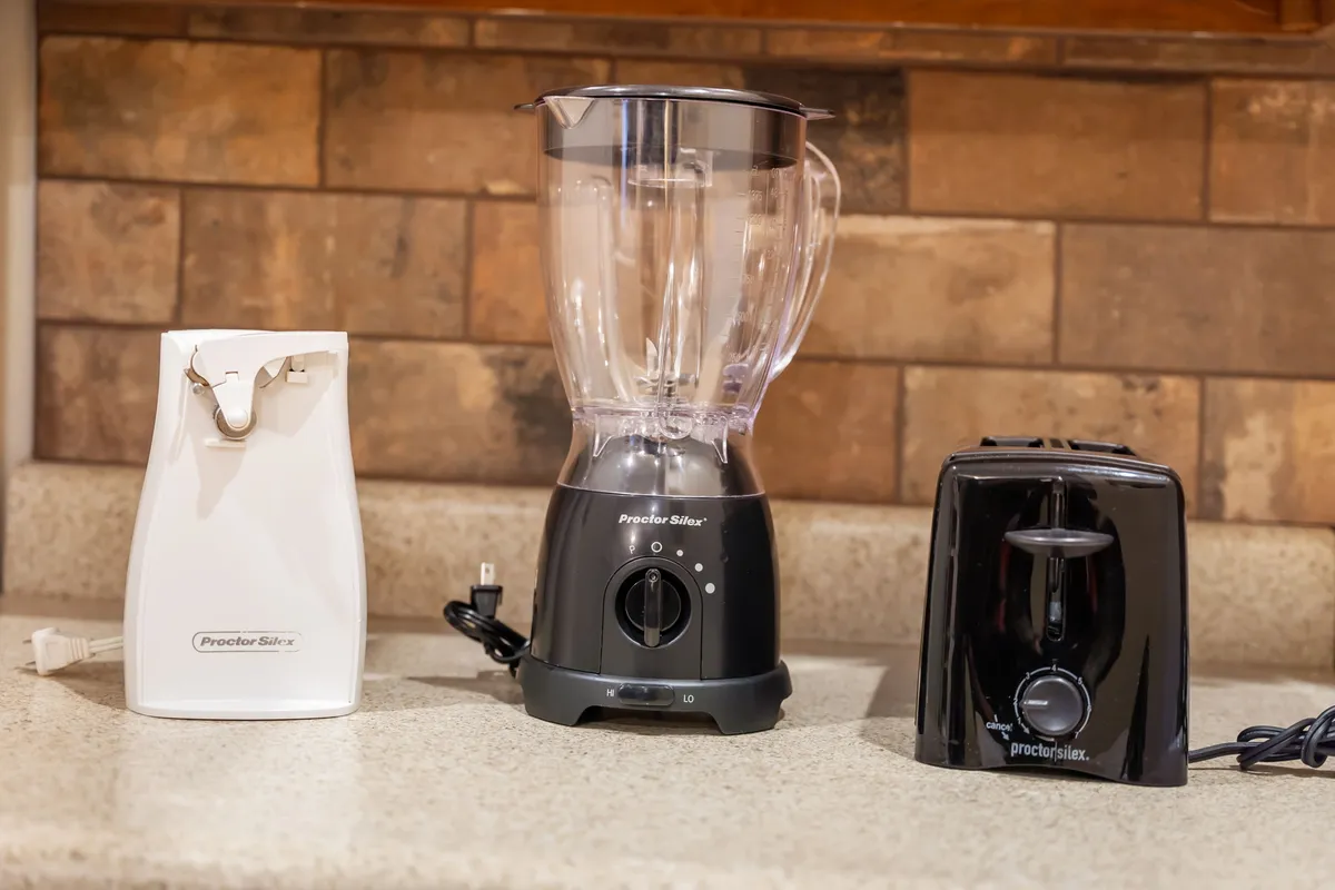A practical kitchen scene focused on small appliances like a blender, toaster, and can opener neatly arranged on the counter, suggesting everyday cooking and homey convenience.